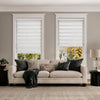 White light filtering zebra shades on two living room windows above a beige sofa