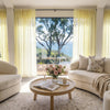 Joydeco custom sheer curtains in pale yellow, framing a serene ocean view in an airy living room.